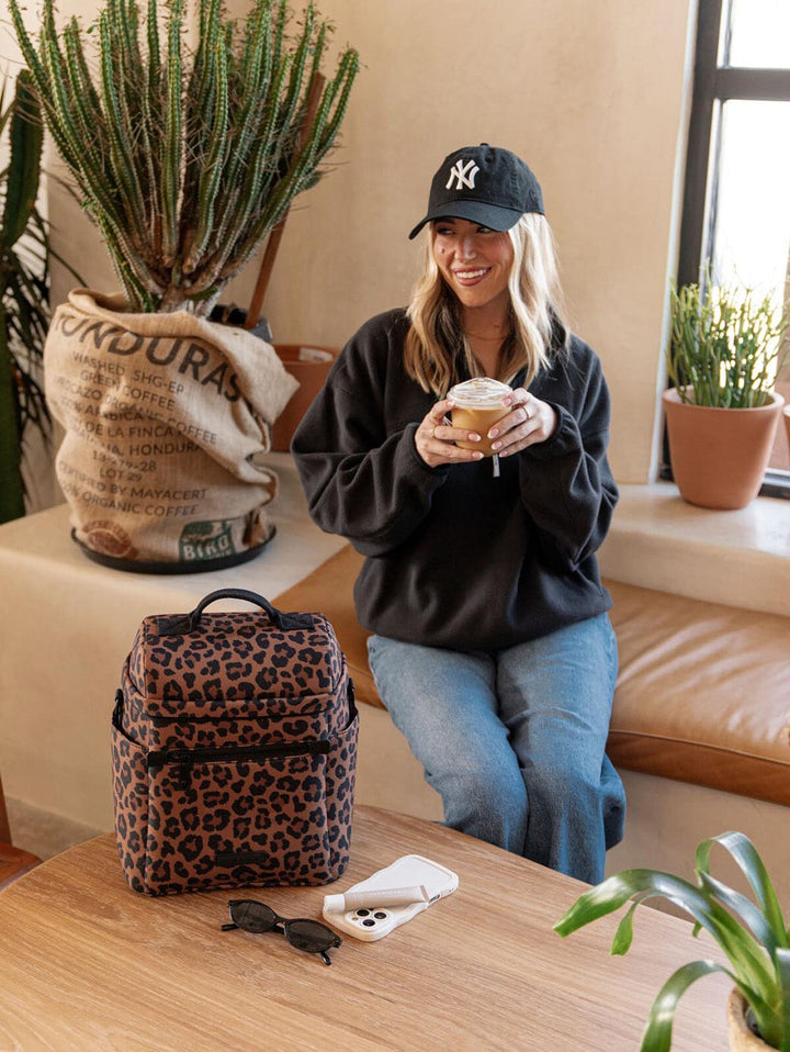 Woman holding a coffee cup with a leopard print lunch bag and plants.
