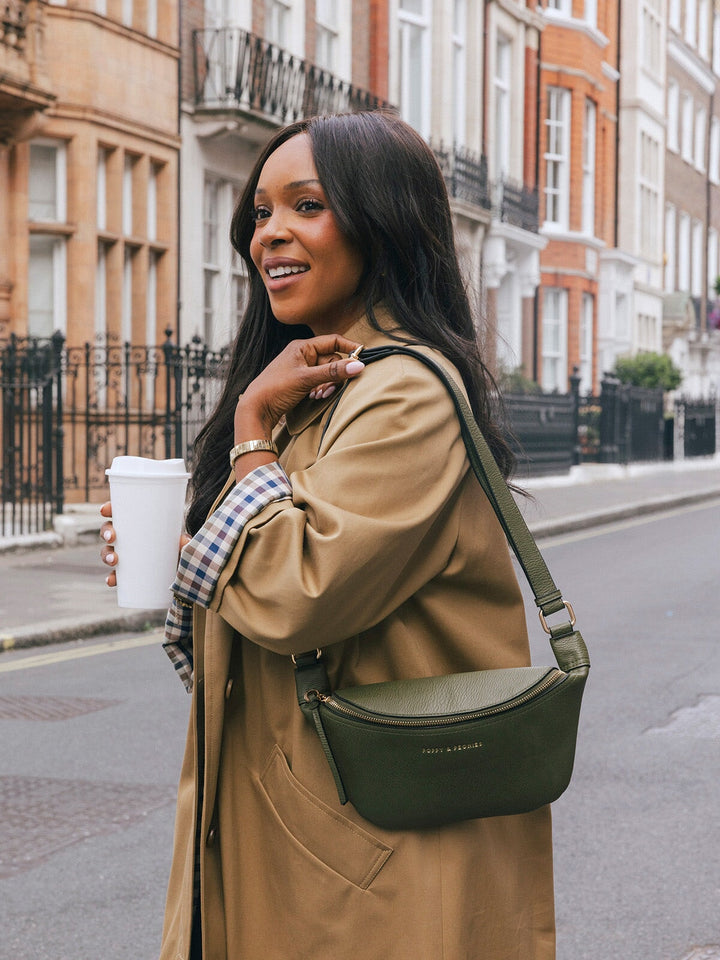 Woman wearing the Poppy & Peonies The Sidekick in Olive as a crossbody while holding a takeaway cup on a city street.