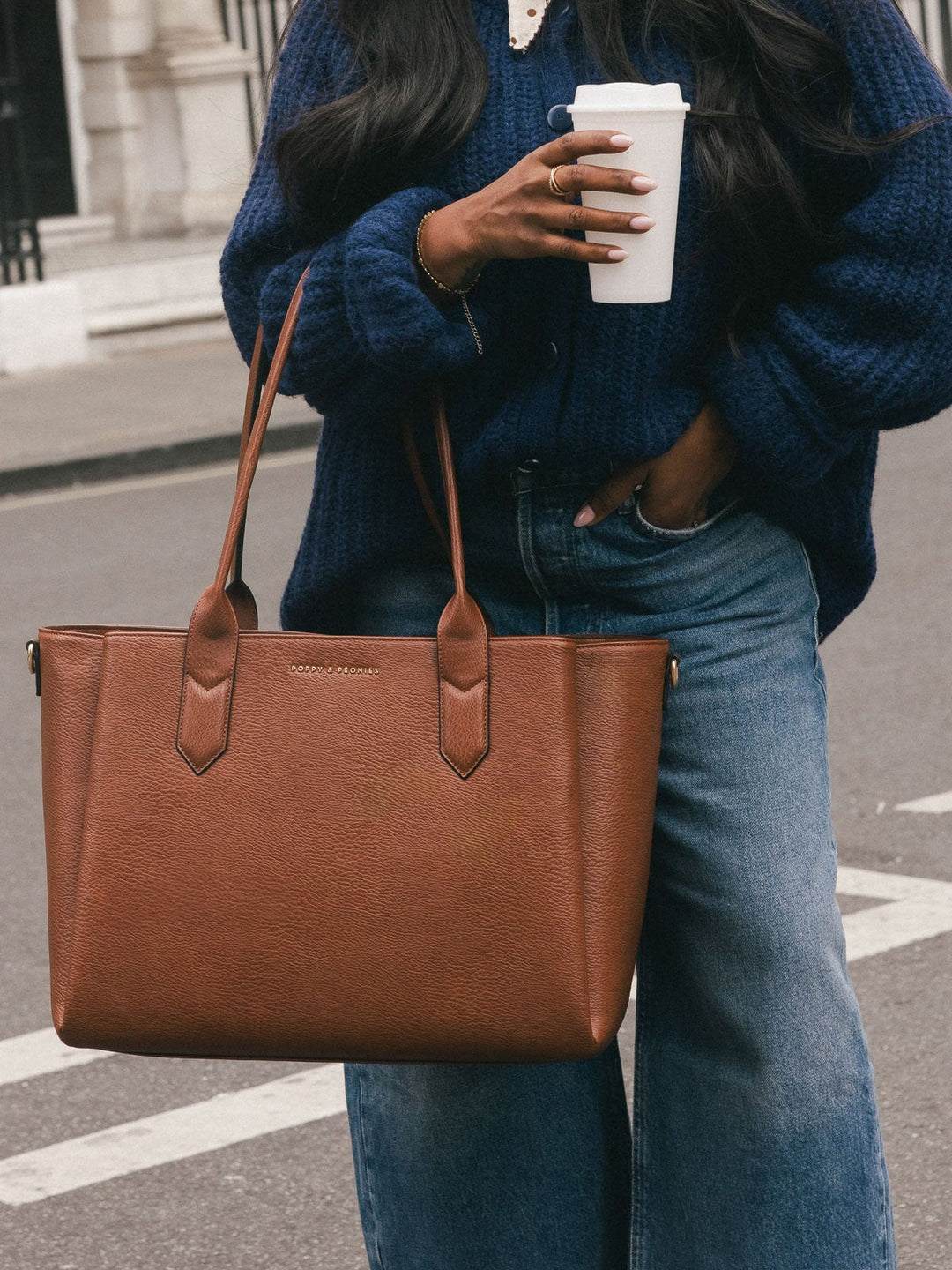 Close-up of the Poppy & Peonies Double Duty Tote in Chestnut carried by the top handles with a coffee in hand.