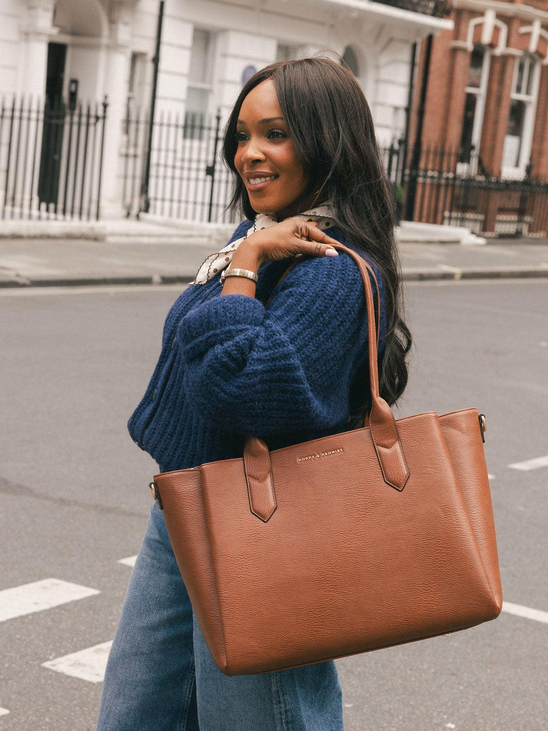 Woman carrying the Poppy & Peonies Double Duty Tote in Chestnut by the top handles over her shoulder on a city street.