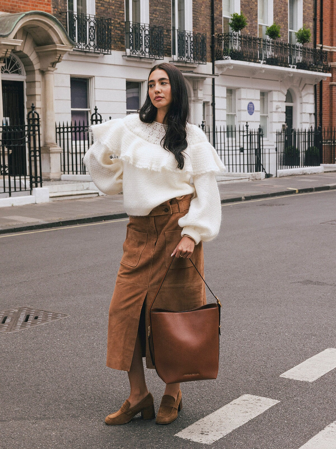 Woman carrying the Poppy & Peonies The Bucket Bag in Chestnut by the shoulder strap while standing on a London street.