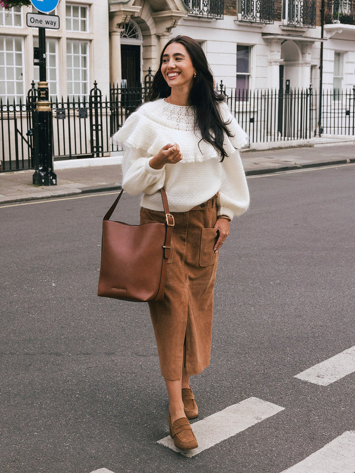Woman carrying the Poppy & Peonies The Bucket Bag in Chestnut by the shoulder strap while walking on a city street.