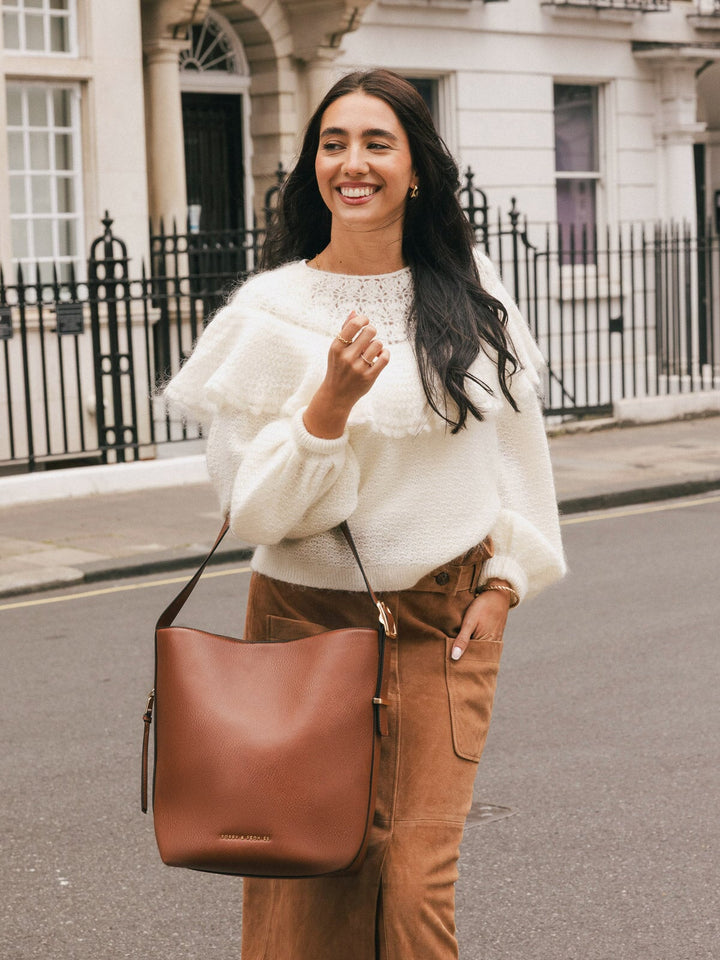 Lifestyle shot of a woman wearing the Poppy & Peonies Bucket Bag in Chestnut on her arm while walking along a city street.