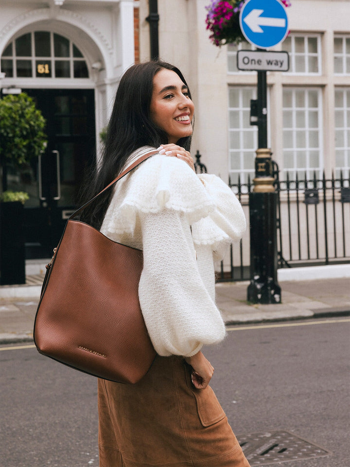 Close-up of woman carrying the Poppy & Peonies The Bucket Bag in Chestnut over her shoulder while smiling on a city street.