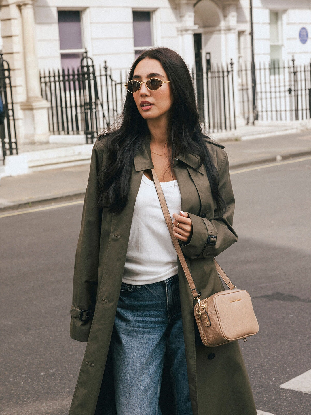 Woman wearing the Poppy & Peonies 24/7 Crossbody in Taupe at her side while standing on a city street.