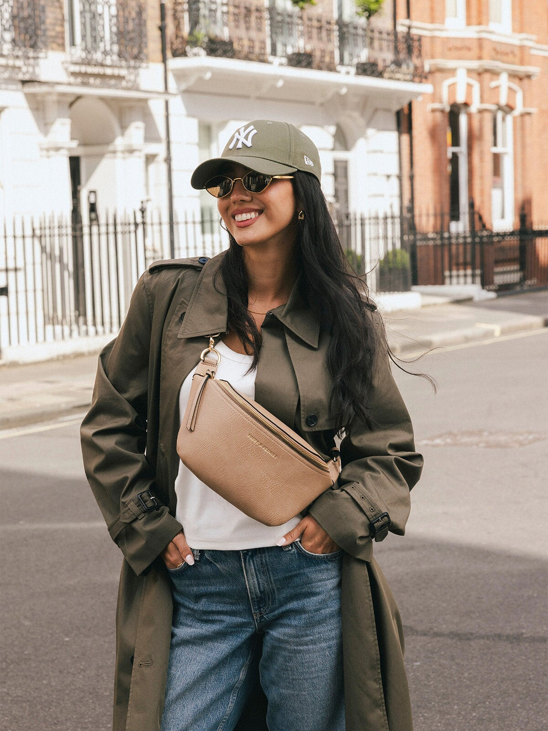 Woman wearing the Poppy & Peonies The Sidekick in Taupe across her chest while smiling on a city street.