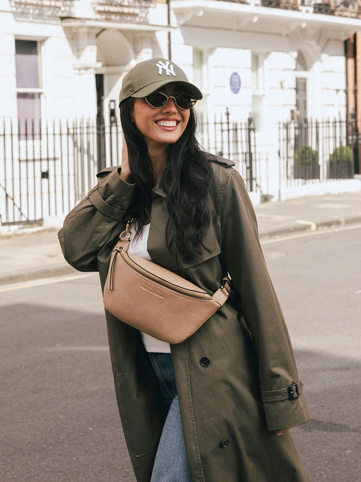 Woman wearing the Poppy & Peonies The Sidekick in Taupe across her chest while smiling on a city street.