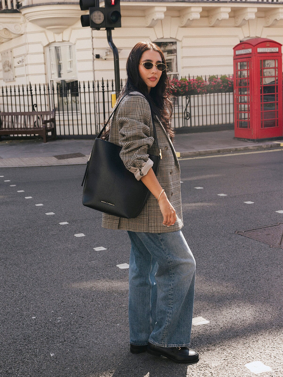 Woman walking with the Poppy & Peonies The Bucket Bag in Black carried over her shoulder on a London street.