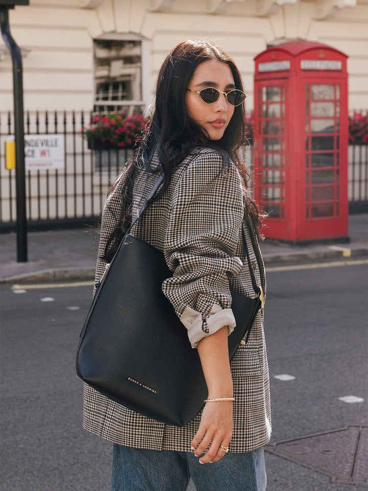 Woman wearing the Poppy & Peonies The Bucket Bag in Black over her shoulder while walking on a London street.