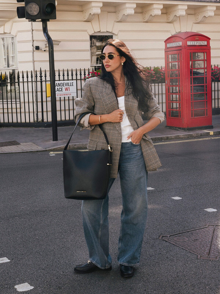 Woman carrying the Poppy & Peonies The Bucket Bag in Black over her shoulder while standing on a city street.