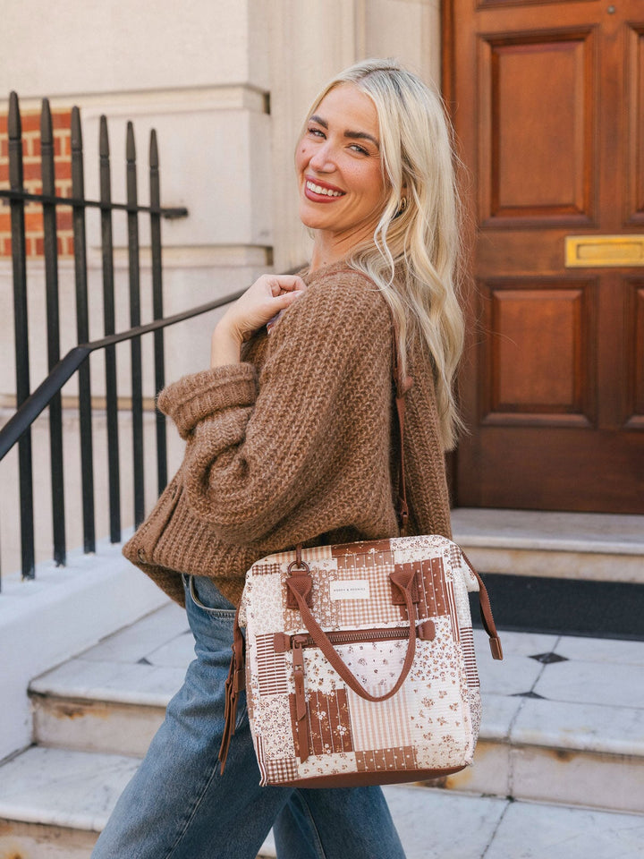Lifestyle shot of a woman wearing the Poppy & Peonies Lunch Bag in Brown Patchwork over the shoulder while posing outside a building entrance.