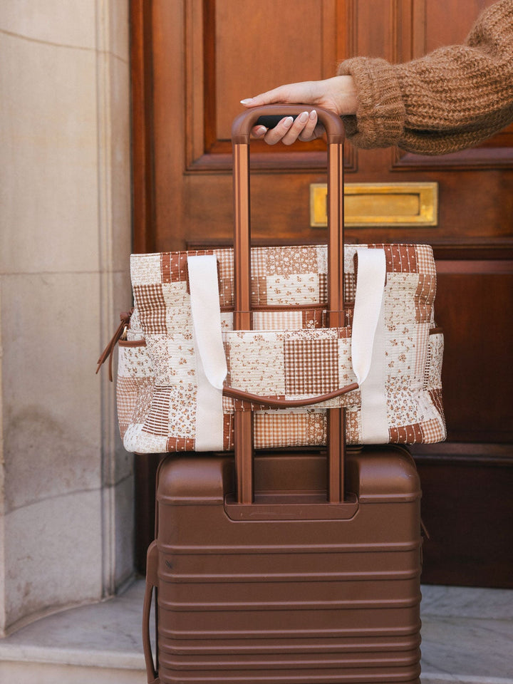 Close-up product-focused shot of the Poppy & Peonies Mini Voyager in Brown Patchwork secured over the handle of rolling luggage.