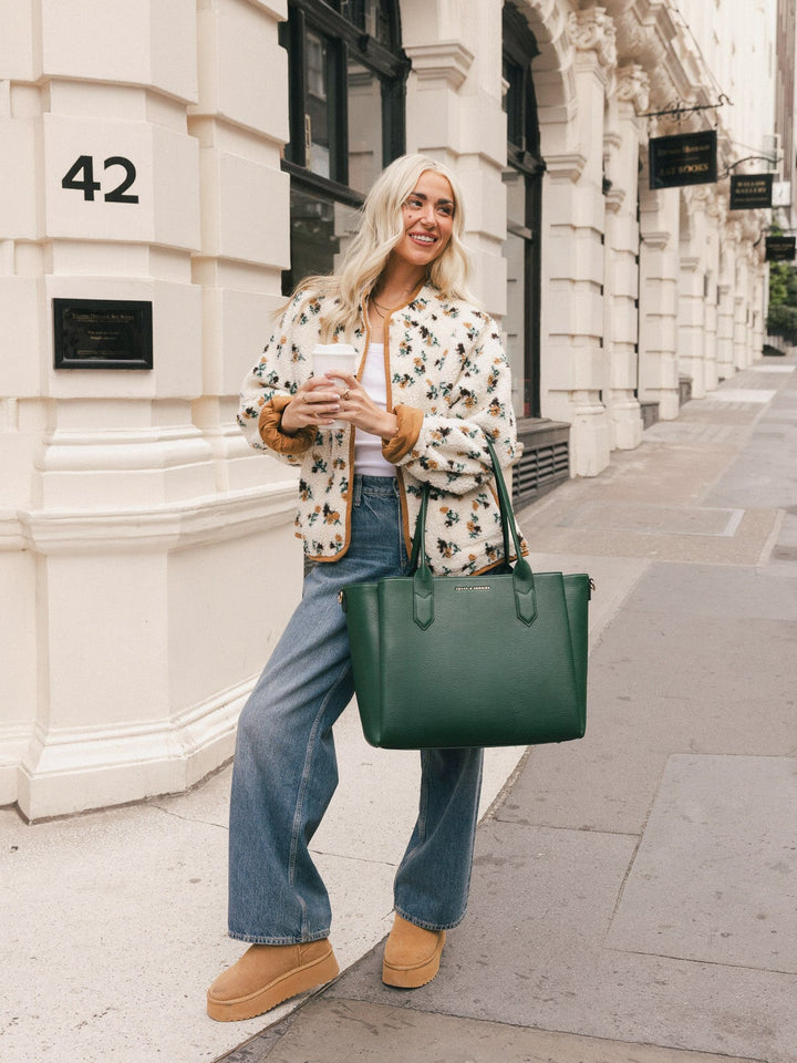 Woman carrying the Poppy & Peonies Double Duty Tote in Heritage Green by the top handles while walking through the city.