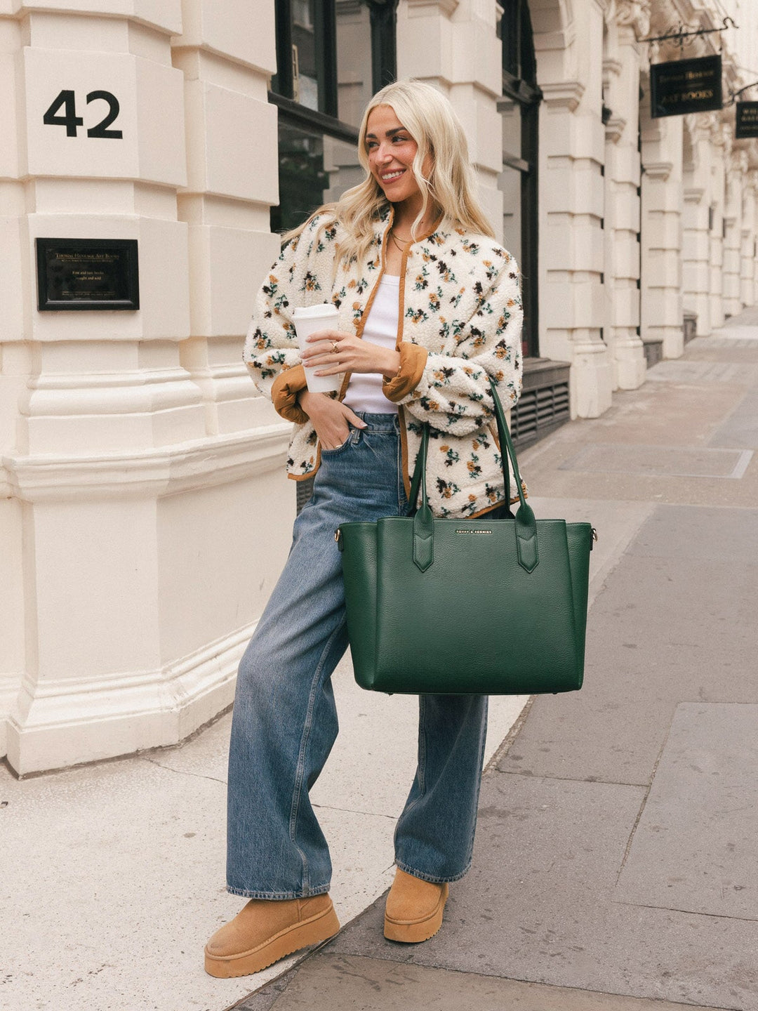 Woman carrying the Poppy & Peonies Double Duty Tote in Heritage Green by the top handles while holding a takeaway coffee.