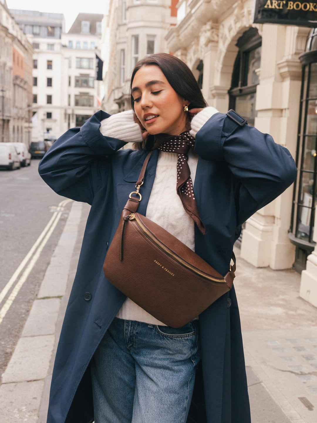 Lifestyle shot of a woman wearing the Poppy & Peonies Large Sidekick in Espresso crossbody while adjusting her hair.