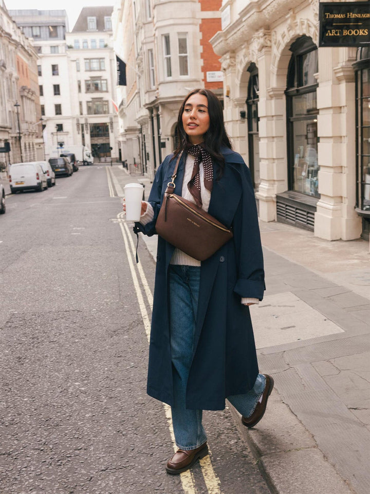 Full-body lifestyle shot of a woman wearing the Poppy & Peonies Large Sidekick in Espresso crossbody while holding a takeaway coffee.