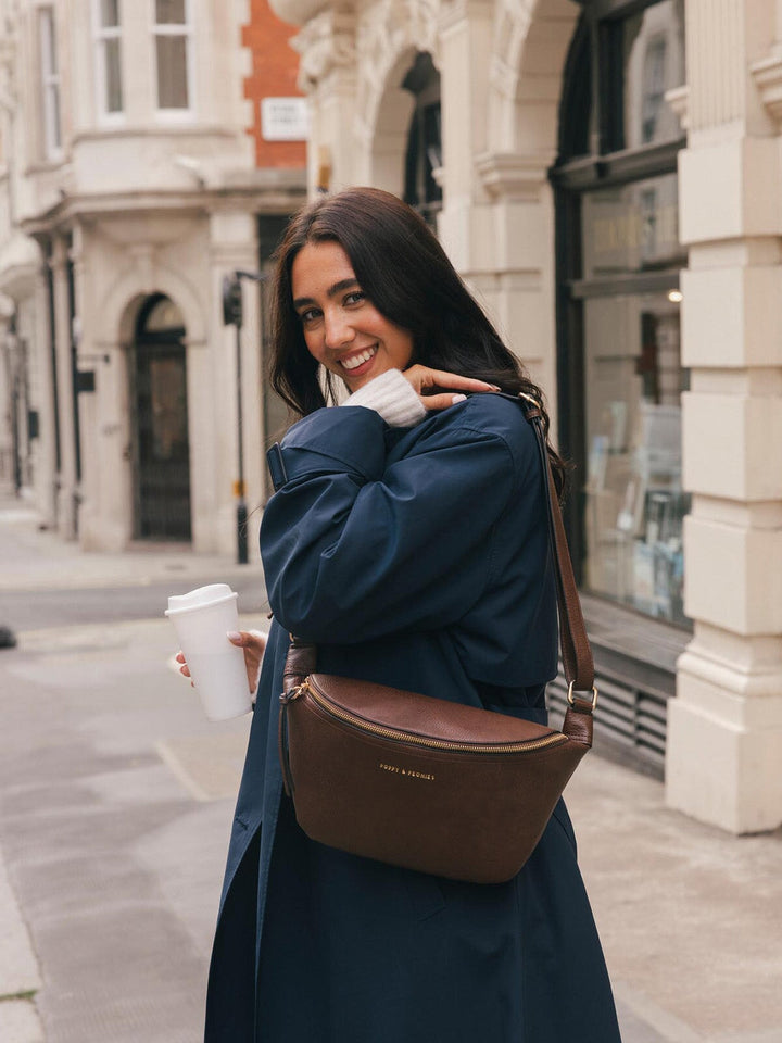 Lifestyle shot of a woman wearing the Poppy & Peonies Large Sidekick in Espresso crossbody while holding a takeaway coffee.
