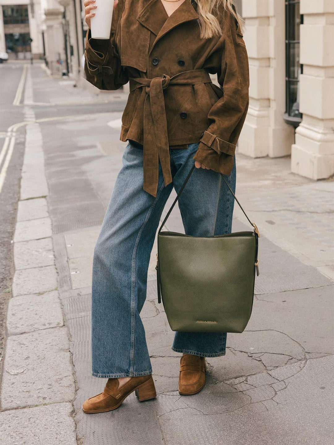 Product-focused lifestyle shot of the Poppy & Peonies Bucket Bag in Olive carried by the shoulder strap at the model’s side.