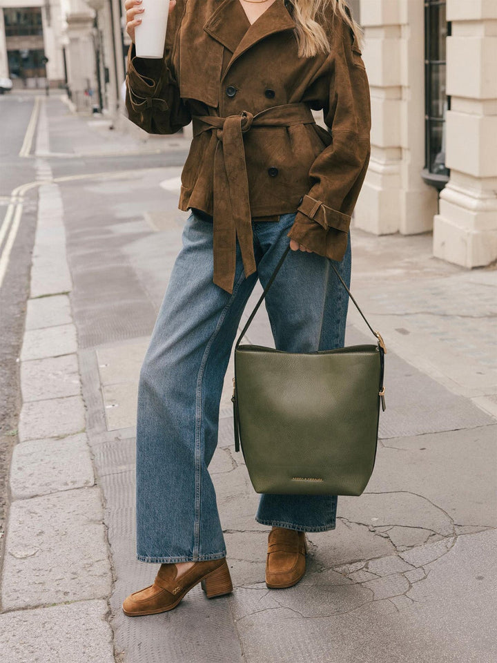 Product-focused lifestyle shot of the Poppy & Peonies Bucket Bag in Olive carried by the shoulder strap at the model’s side.