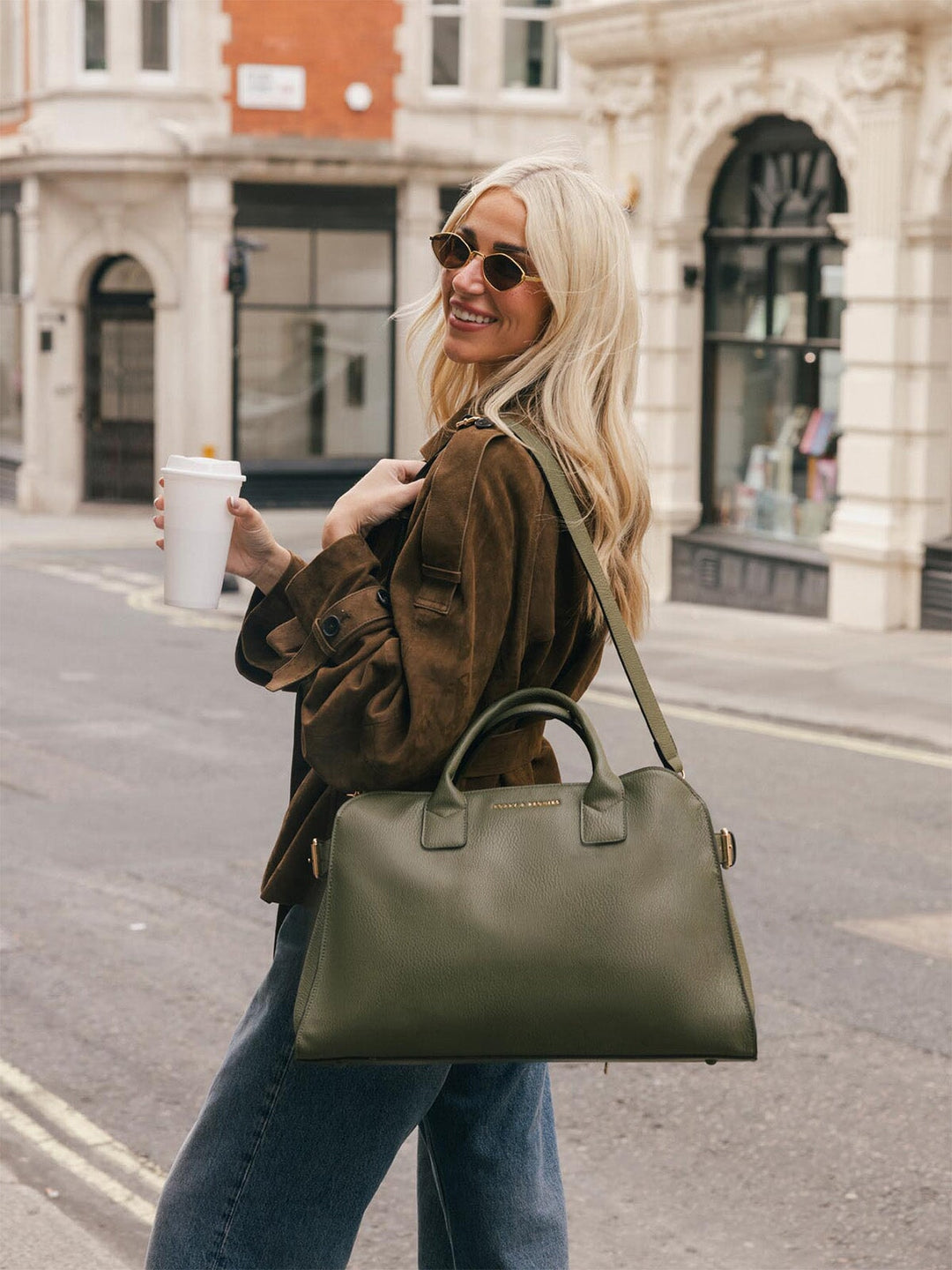 Lifestyle shot of a woman carrying the Poppy & Peonies Uptown Tote in Olive by the top handles while walking along a city street.
