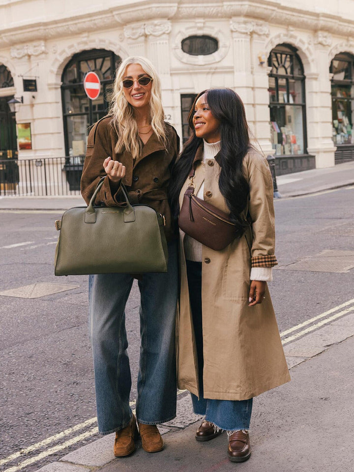 Full-body lifestyle shot of two women posing together on a city street with the Poppy & Peonies Uptown Tote in Olive.