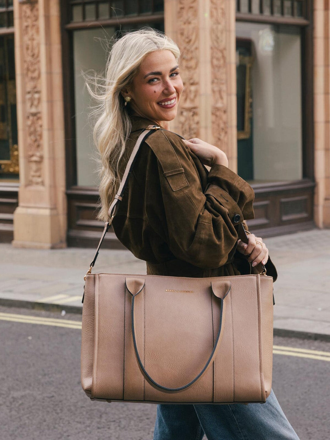 Woman wearing the Poppy & Peonies Multitasker in Taupe over her shoulder while posing on a city street.