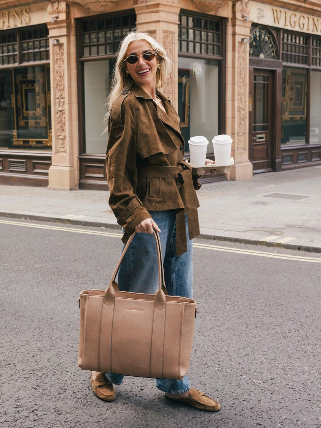 Woman walking with the Poppy & Peonies Multitasker in Taupe carried by the top handles on a city street.