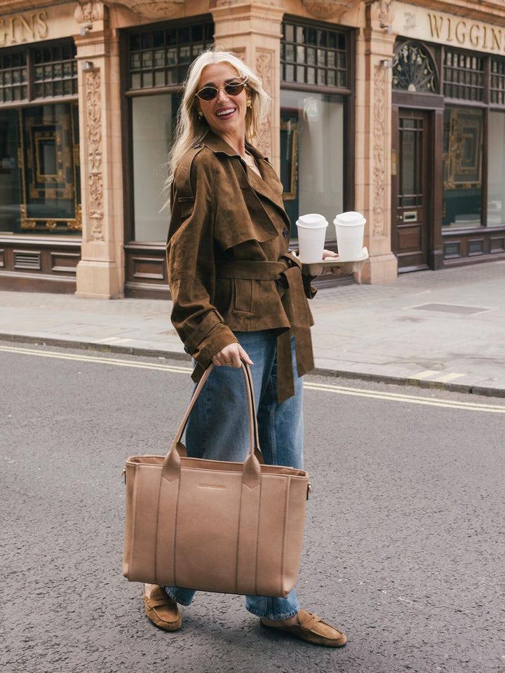 Woman walking with the Poppy & Peonies Multitasker in Taupe carried by the top handles on a city street.