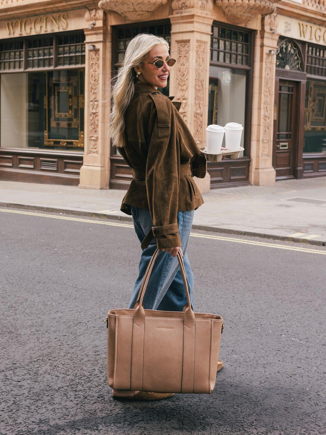 Woman carrying the Poppy & Peonies Multitasker in Taupe by the top handles while walking on a city street.