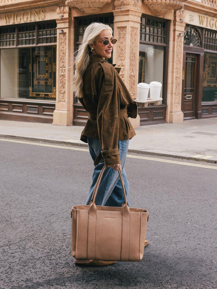 Woman carrying the Poppy & Peonies Multitasker in Taupe by the top handles while walking on a city street.