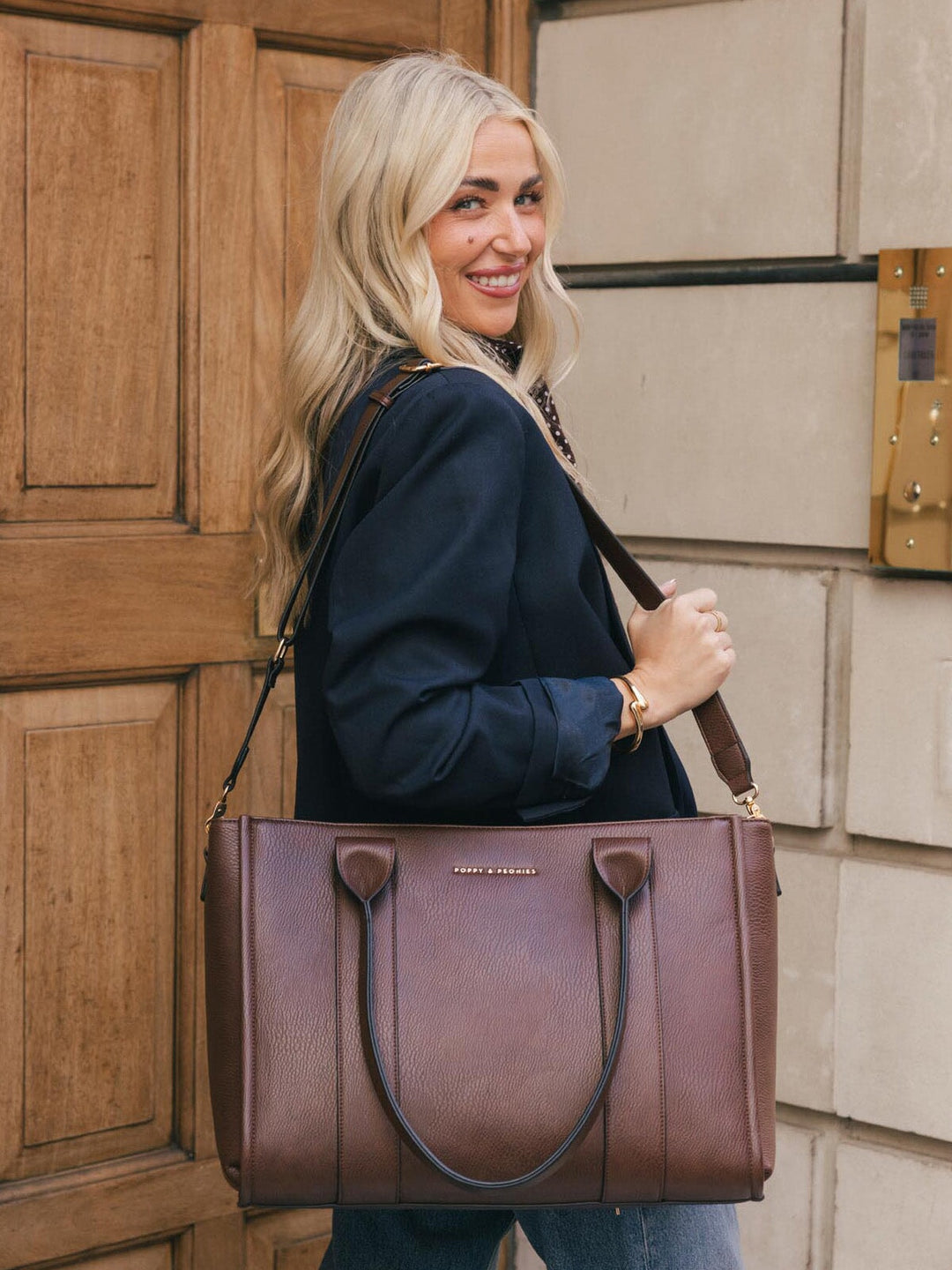 Woman smiling while carrying the Poppy & Peonies Multitasker in Espresso over her shoulder.