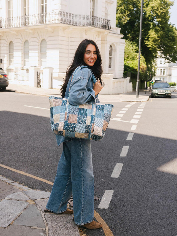 Woman carrying the Poppy & Peonies Daydreamer Tote in Navy Patchwork over her shoulder while walking on a city street.