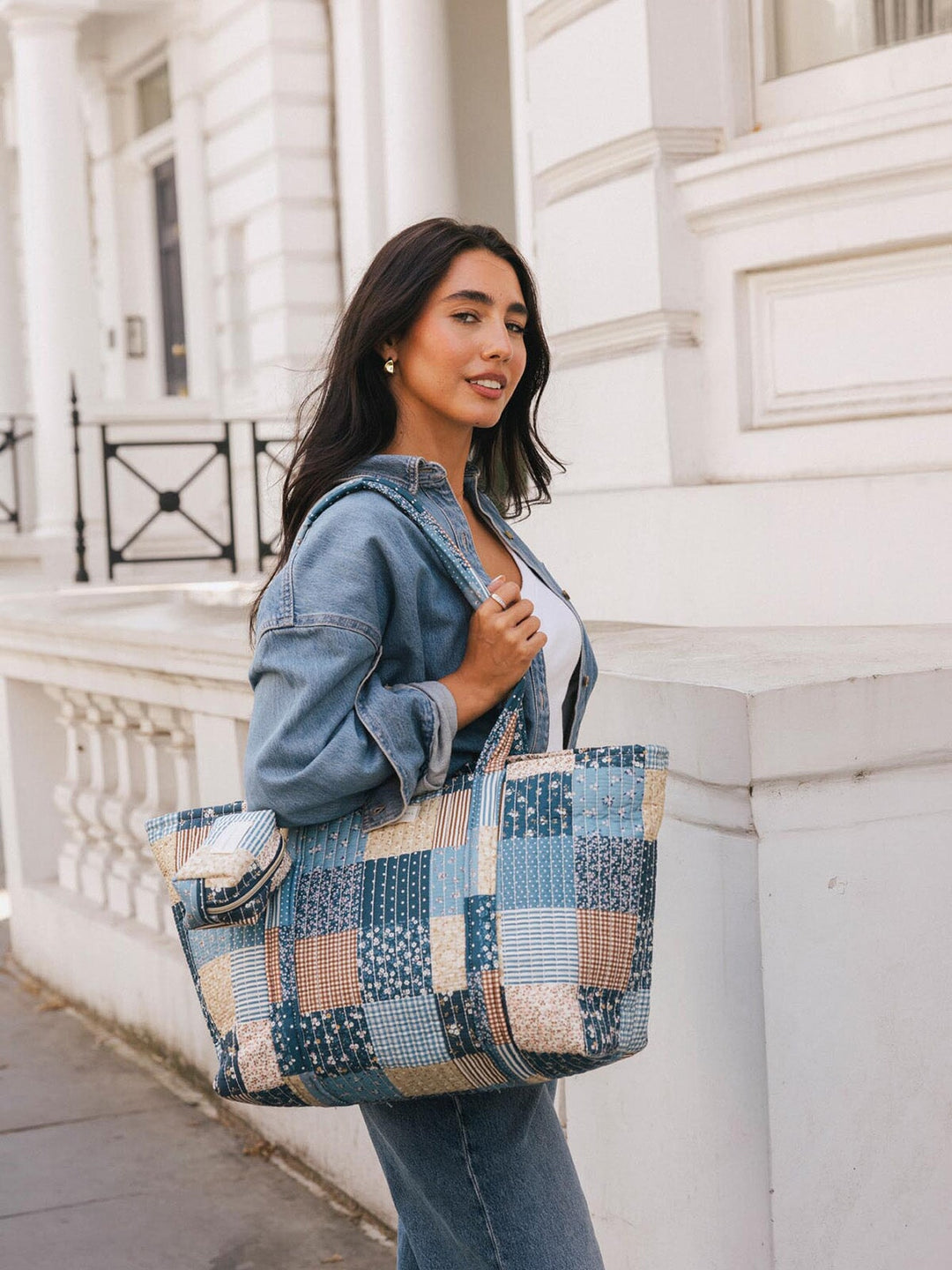 Woman carrying the Poppy & Peonies Daydreamer Tote in Navy Patchwork over her shoulder, showing the patchwork print and tag along bag charm. 