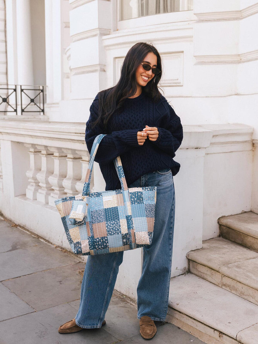 Woman carrying the Poppy & Peonies Daydreamer Tote in Navy Patchwork by the top handles while standing on a city sidewalk.