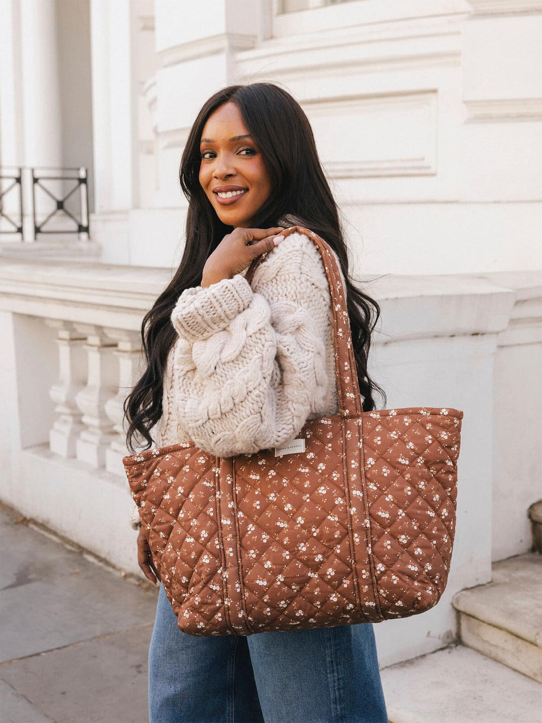 Woman carrying the Poppy & Peonies Daydreamer Tote in Brown Floral over her shoulder, showing the quilted floral print and spacious tote silhouette.
