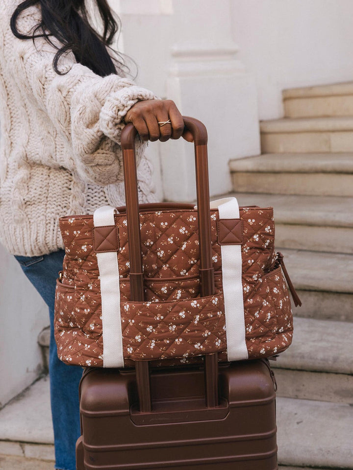 Close-up of the Poppy & Peonies Mini Voyager in Brown Floral secured to the handle of a rolling suitcase.