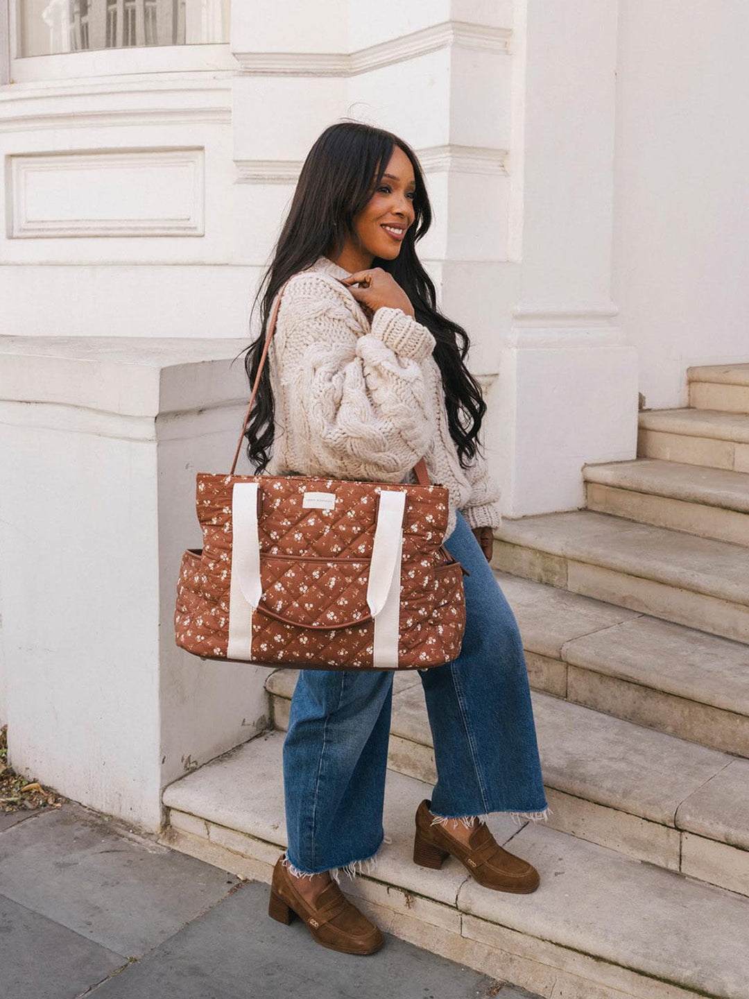 Woman carrying the Poppy & Peonies Mini Voyager in Brown Floral by the top handles while standing on outdoor steps.