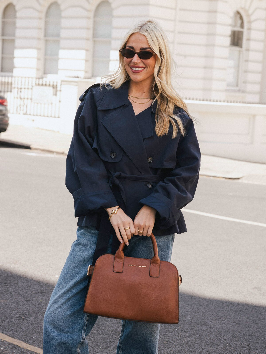 Woman holding the Poppy & Peonies Mini Uptown Tote in Chestnut by the top handles while smiling outdoors.