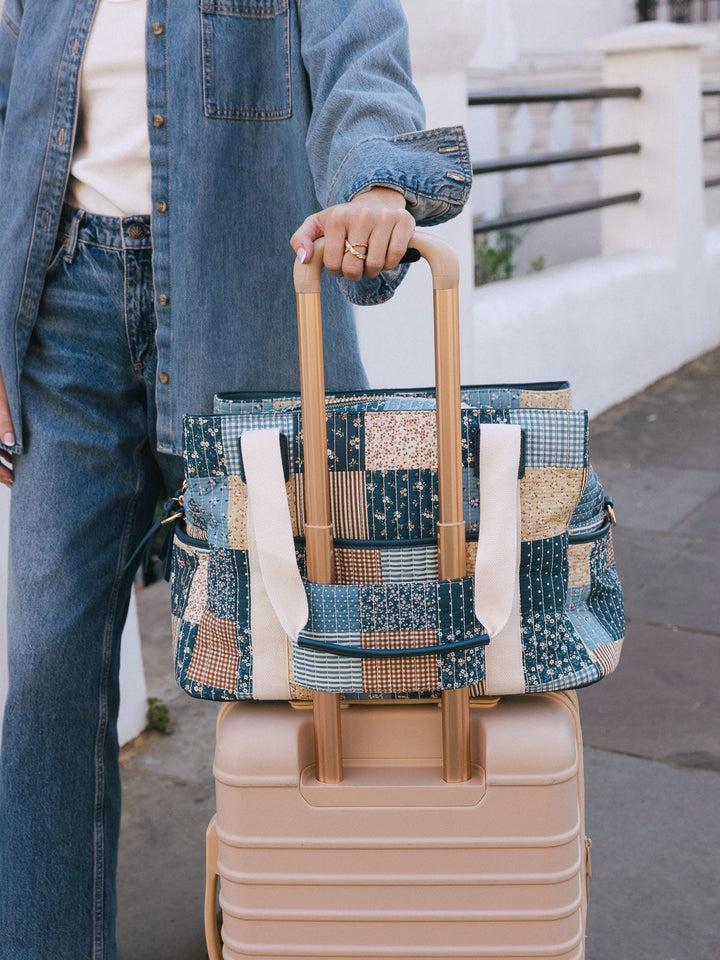 Close-up of the Poppy & Peonies Mini Voyager in Navy Patchwork secured over the handle of a rolling suitcase.