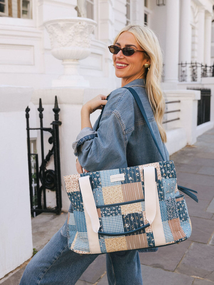 Woman carrying the Poppy & Peonies Mini Voyager in Navy Patchwork over her shoulder while smiling outdoors.