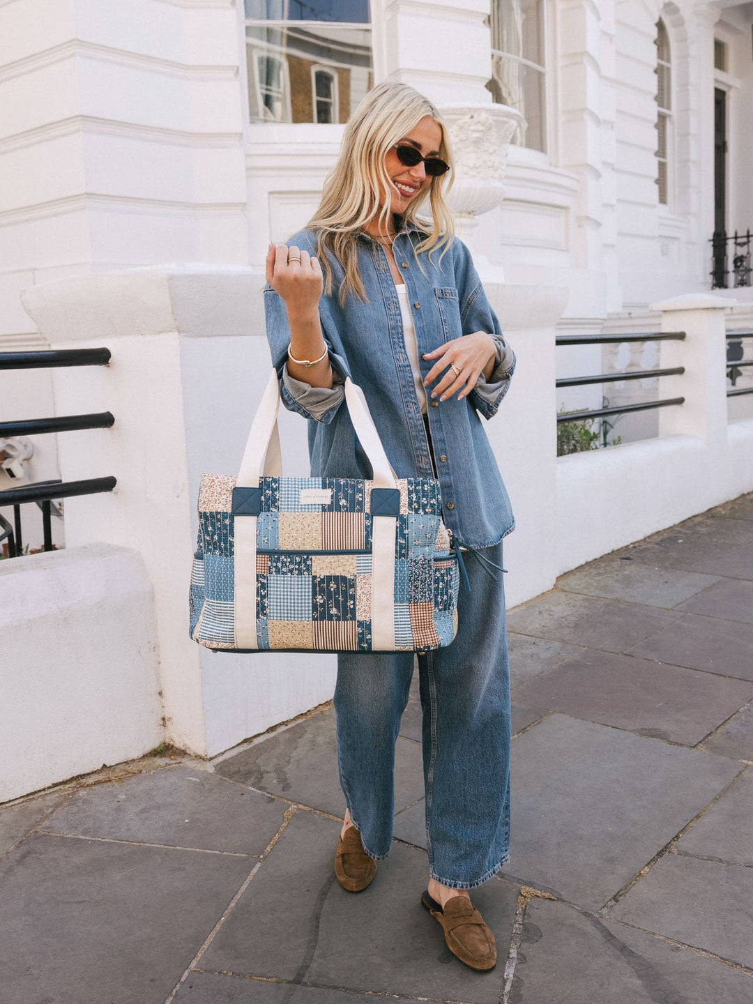 Woman carrying the Poppy & Peonies Mini Voyager in Navy Patchwork by the top handles while standing outdoors.