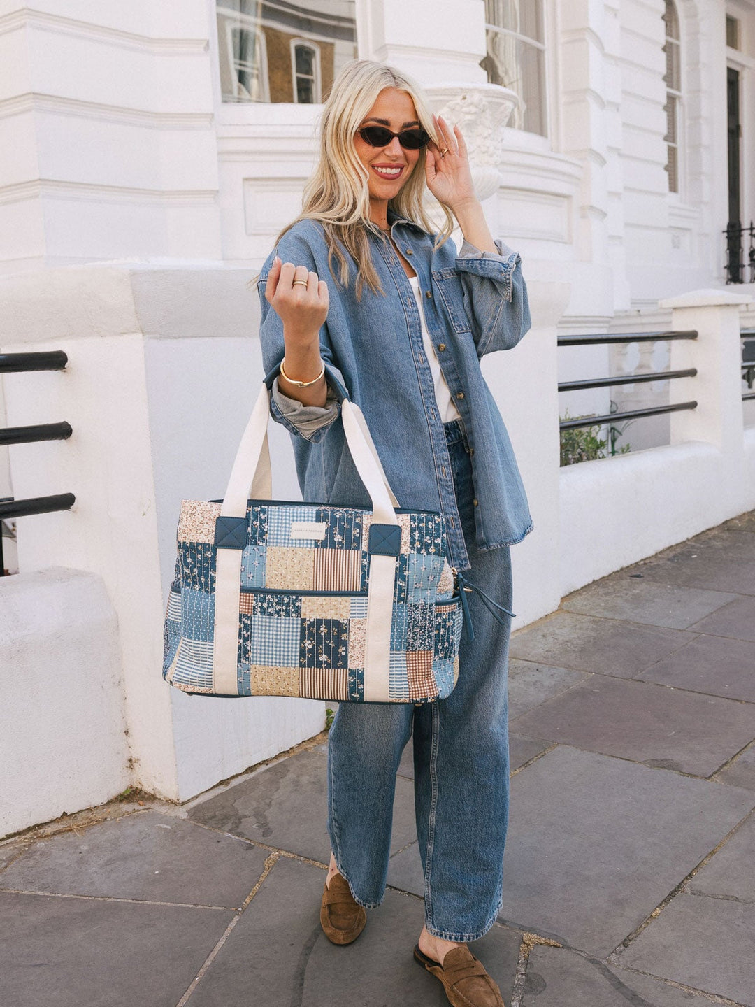 Woman holding the Poppy & Peonies Mini Voyager in Navy Patchwork by the top handles while posing on a city sidewalk.