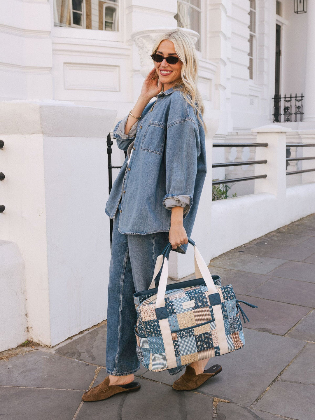 Woman carrying the Poppy & Peonies Mini Voyager in Navy Patchwork by the top handles while walking outdoors.
