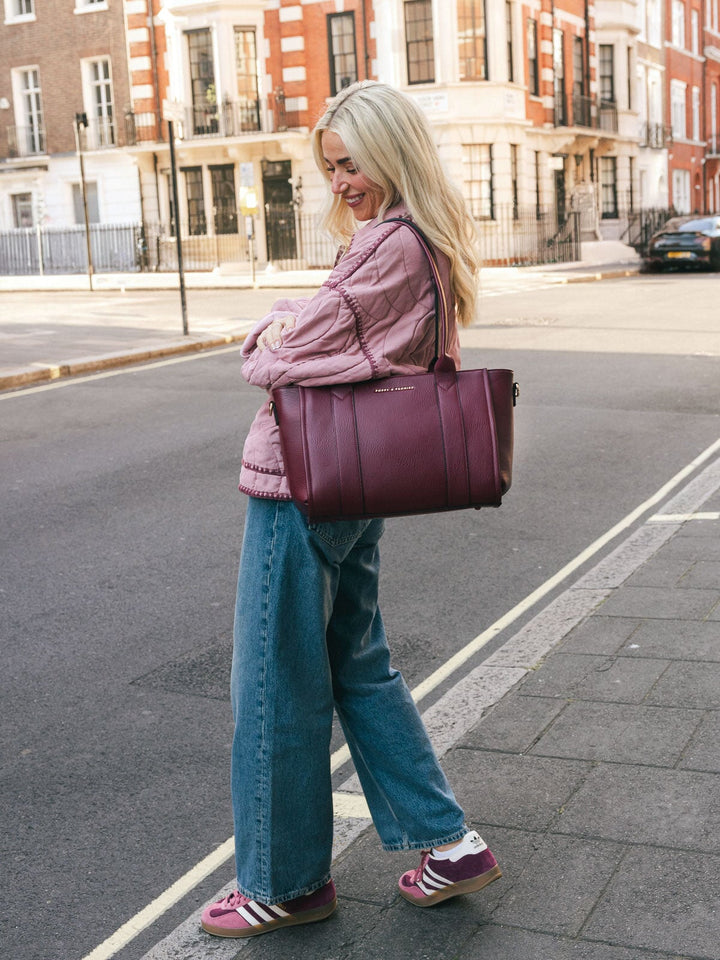 Woman carrying the Poppy & Peonies Small Multitasker in Berry over her shoulder while walking along a city street.
