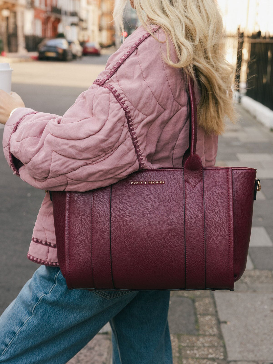 Close-up of a woman carrying the Poppy & Peonies Small Multitasker in Berry over her shoulder while walking on a city street.