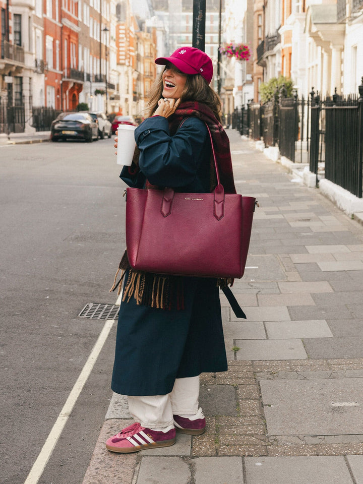 Woman carrying the Poppy & Peonies Double Duty Tote in Berry over the shoulder with the top handles while walking through the city.