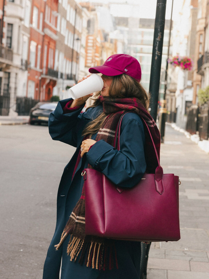 Close-up of woman carrying the Poppy & Peonies Double Duty Tote in Berry over her shoulder while drinking a takeaway coffee.