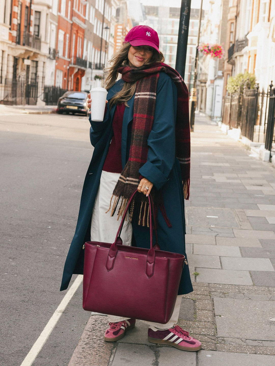 Woman carrying the Poppy & Peonies Double Duty Tote in Berry by the top handles while enjoying coffee on a city street.