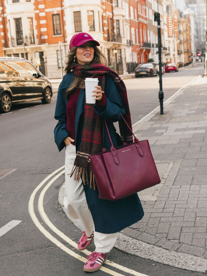 Woman carrying the Poppy & Peonies Double Duty Tote in Berry by the top handles while walking with coffee.