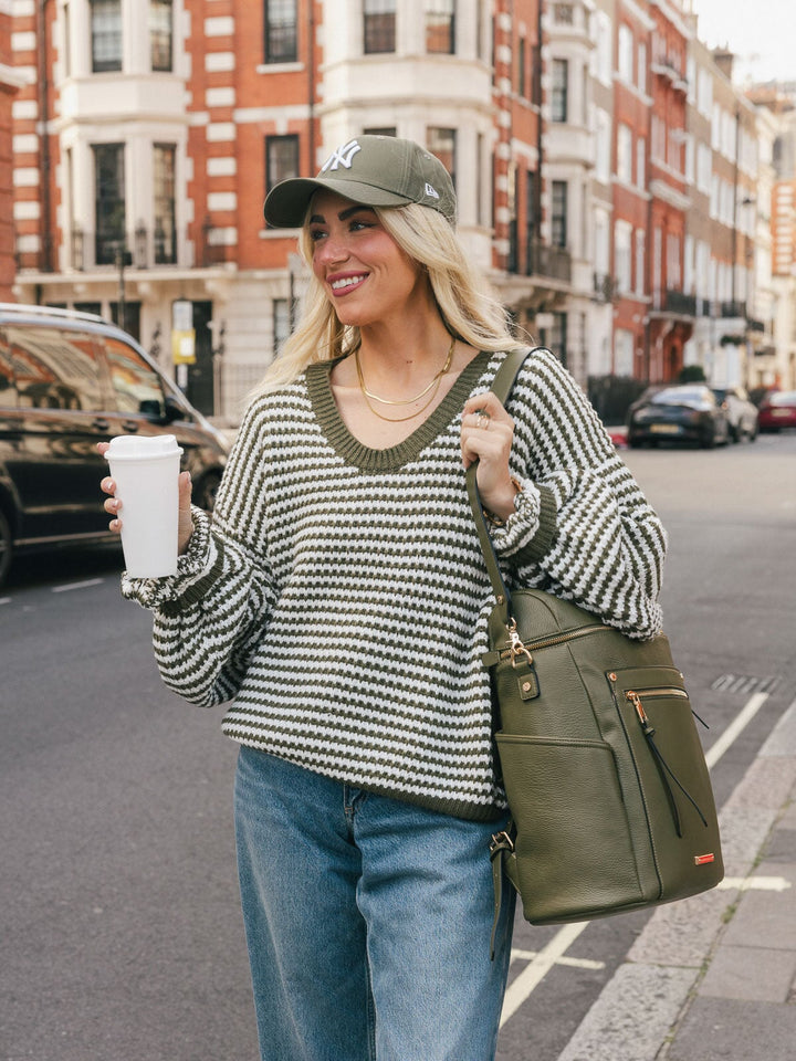 Woman carrying the Poppy & Peonies Commuter Backpack in Olive over one shoulder while smiling and holding a takeaway coffee.
